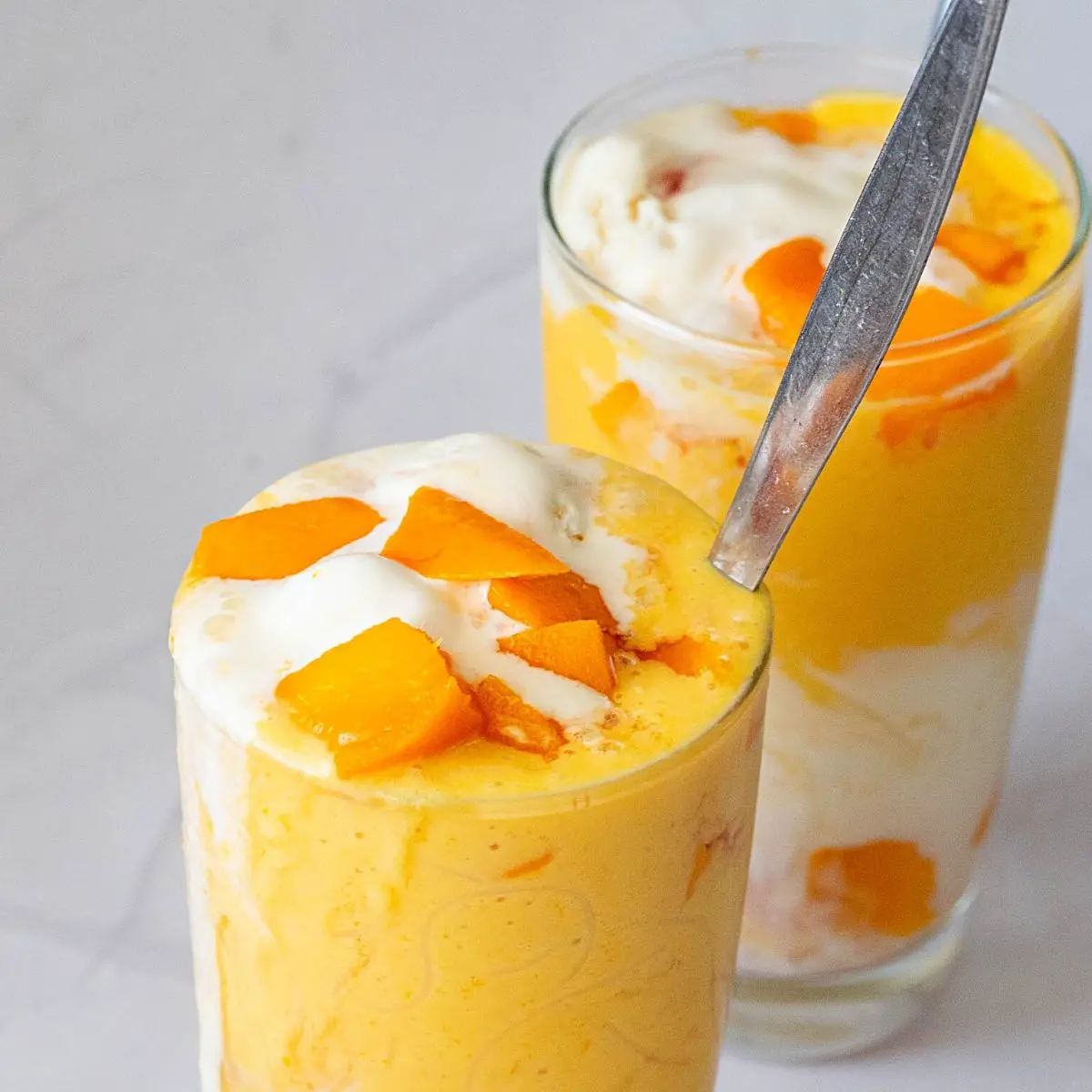 Two glasses with mango pieces in falooda.