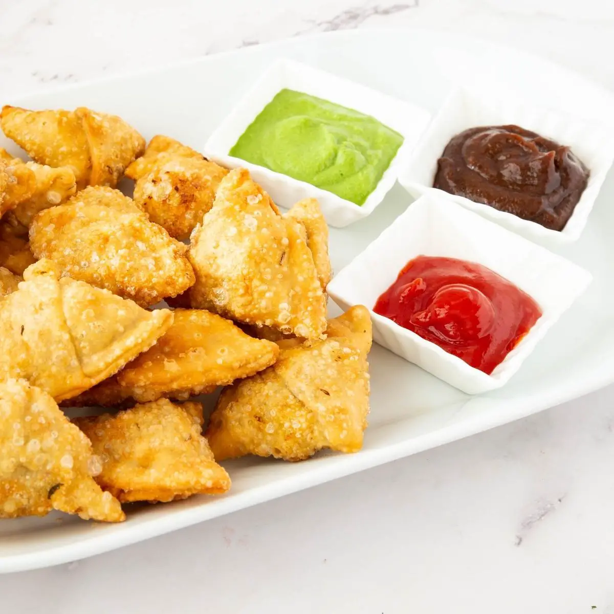 Samosa with sauces on a white plate.