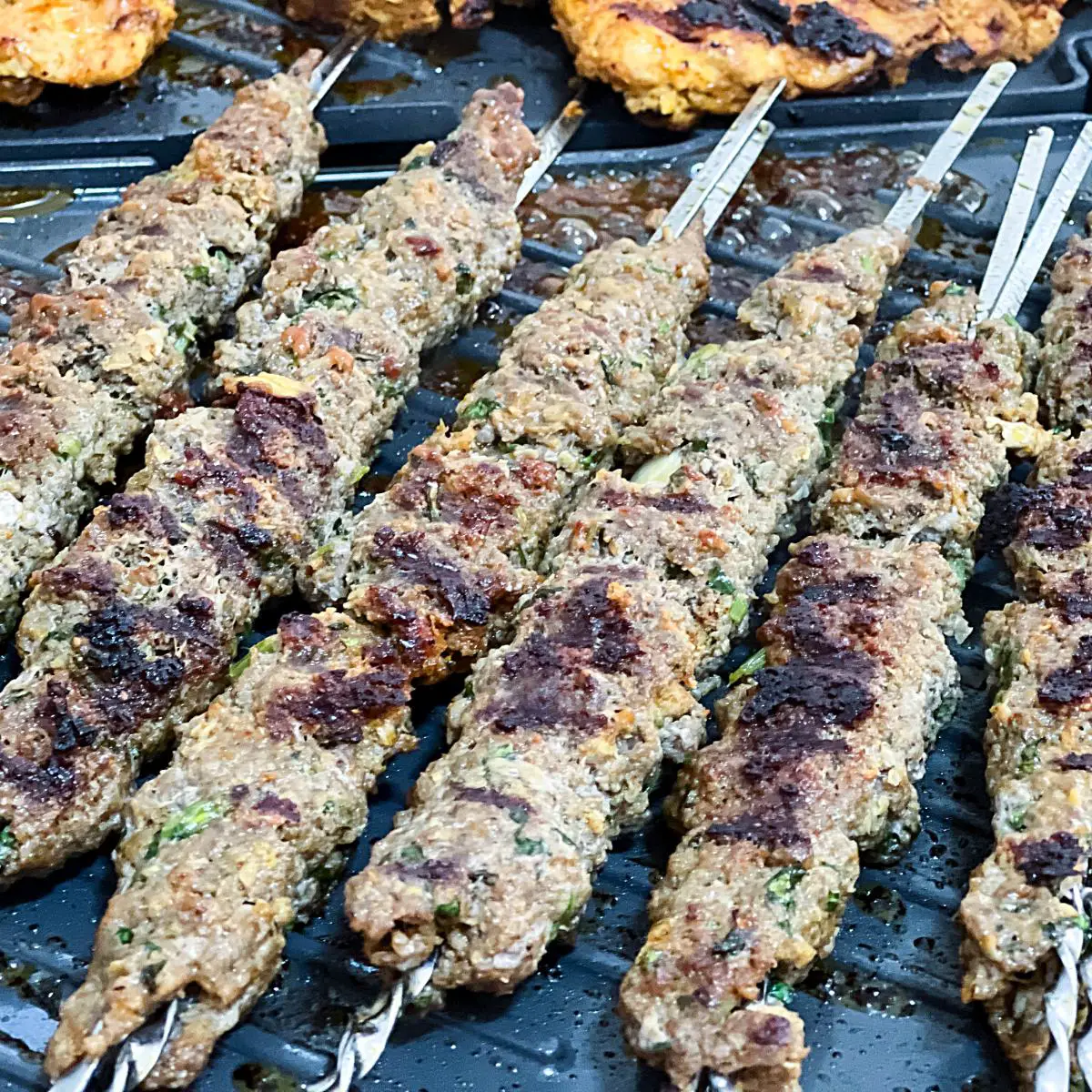 A grill pan with beef on metal skewers.